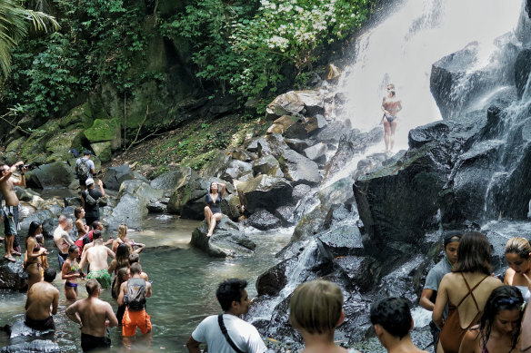 Tourists line up while others pose under the Kato Lampo waterfall in Gianyar, Bali. 