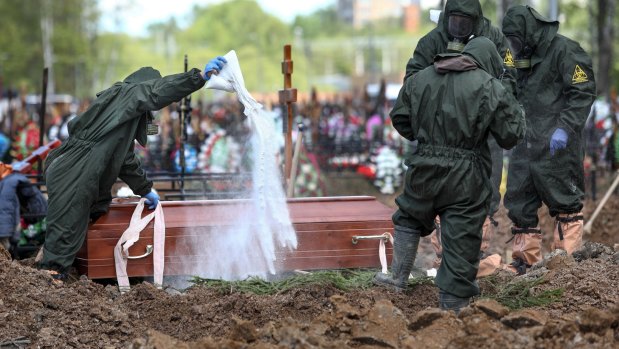 Cemetery workers in protective suits disinfect a grave as they bury a COVID-19 victim in a section of the Butovskoye cemetery reserved for coronavirus victims outside Moscow, Russia. 