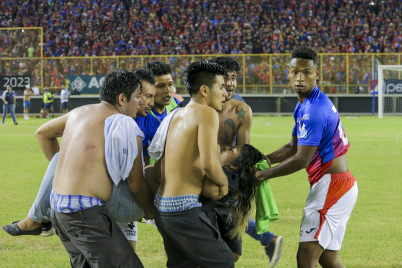 Men and a soccer player carry an injured fan to the field of Cuscatlan stadium in San Salvador, El Salvador, where at least 12 people were killed in a crush.