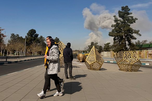 People turn away as a smoke plume rises after an airstrike on Thursday in the Boroujerdi Town area of southern Tehran.