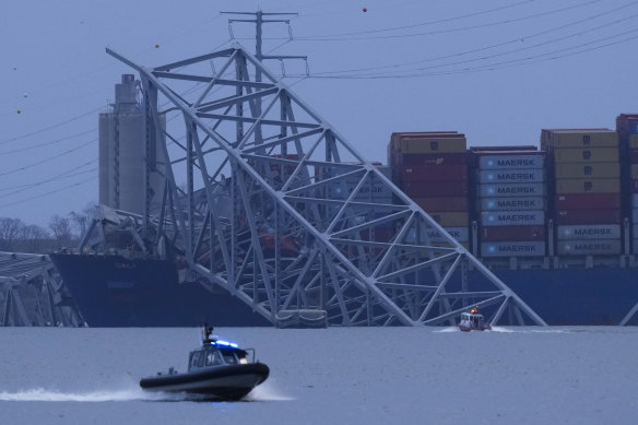 A small boat with flashing lights crosses the water in front of the crashed ship. 