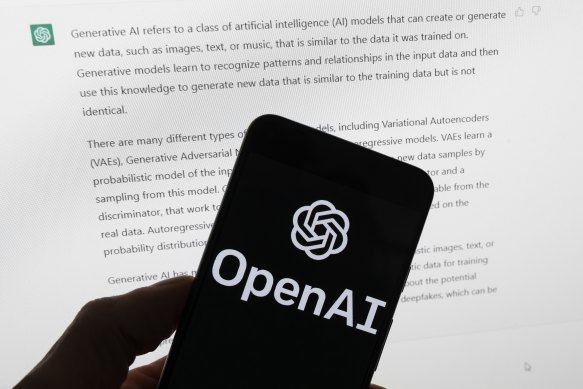The OpenAI logo is seen on a mobile phone in front of a computer screen displaying output from ChatGPT in Boston, US.