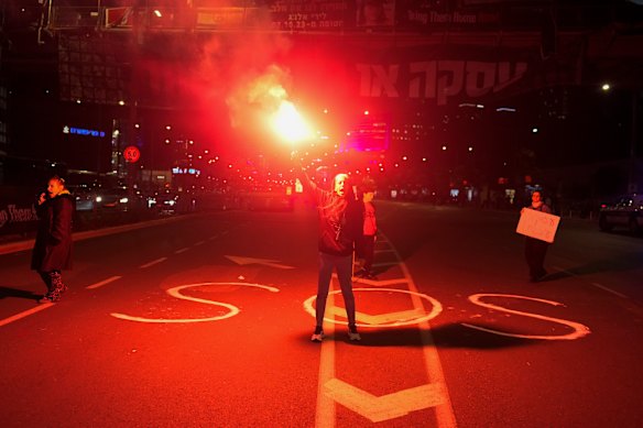 A demonstrator holds up a flare as she stands on a street during a protest calling for a deal to release the hostages held in the Gaza Strip by the Hamas militant group, in Tel Aviv, Israel.
