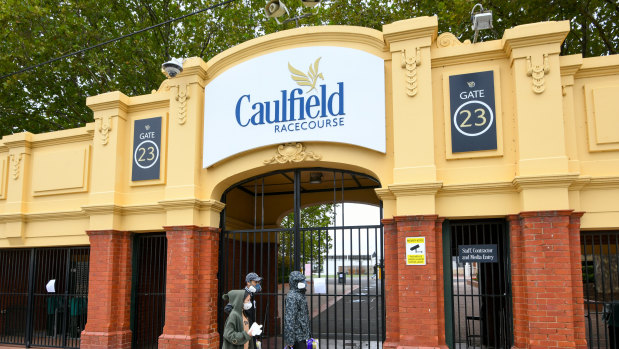 People wearing masks and carrying toilet paper walk past Caulfield Racecourse in Melbourne on Saturday.