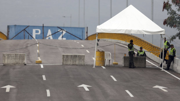Colombian police stand on the Colombian side of the Tienditas International Bridge, which is blocked with a cargo trailer placed by Venezuelan authorities to block humanitarian aid from entering. The word 'peace' is visible on the trailer.