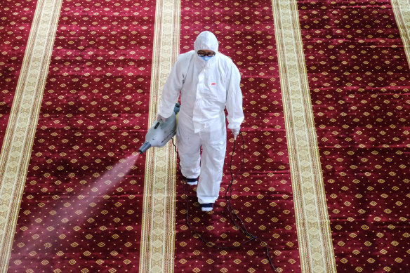 A worker wearing a protective suit and a mask sprays disinfectant at a mosque near Kuala Lumpur, Malaysia.