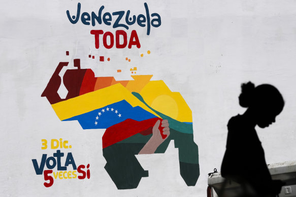 A woman sells fruit in front of a mural of a Venezuelan map with the Essequibo territory (bottom right of map) included and the words “All of Venezuela. Vote yes five time on December 3”, in Caracas.