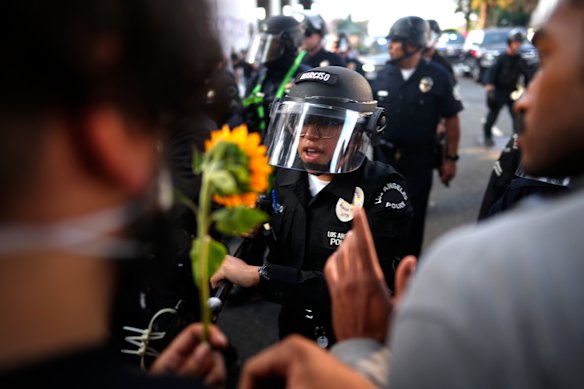A Los Angeles police officer uses a baton to push back a protester offering them a flower in downtown Los Angeles on Monday.