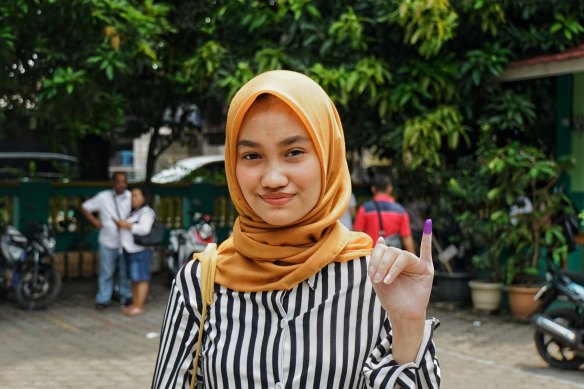Putri Elma, a first-time voter, shows the inked finger proving she has already cast her ballot.