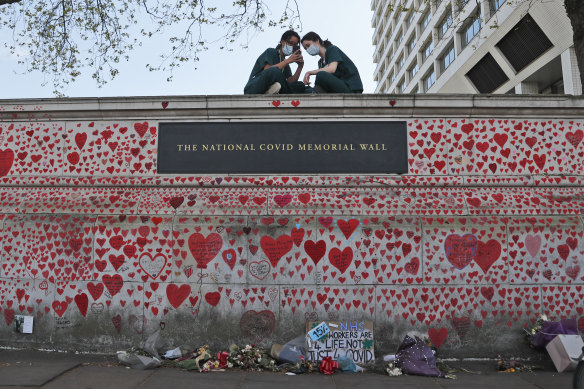 Nurses from the nearby St Thomas’ hospital sit atop the National COVID-19 Memorial Wall in London.