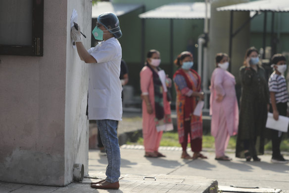 A doctor fills a form, as others wait in a queue for COVID-19 tests in Jammu, India this week. 