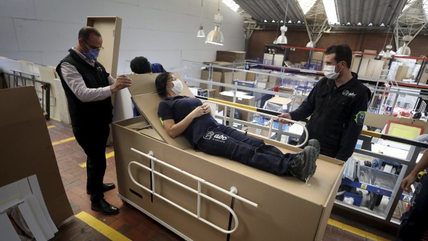 Rodolfo Gomez, left, and his employees demonstrate how their design of a cardboard box can serve as both a hospital bed and a coffin.