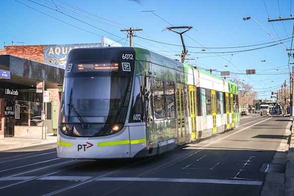 A tram kicks up sand along Plenty Road, outside Moore’s shop.