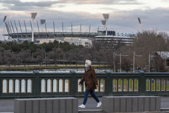 A woman wearing a mask walks along a bridge as she walks past the MCG in August.