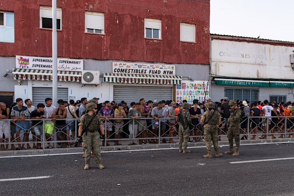 Migrants wait for a shop to open so they can buy food after crossing from Morocco.