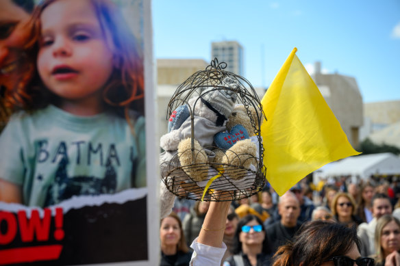 Une femme tient une cage avec des ours en peluche représentant des otages près d'une affiche pour la famille Bibas.