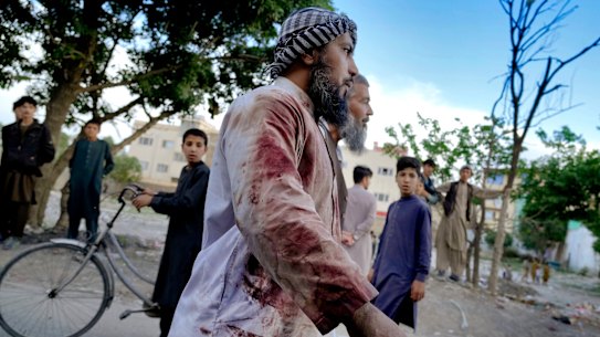 An Afghan blood-stained worshiper walks around the mosque where the explosion took place, in Kabul.
