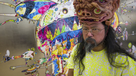 Takashi Murakami, wearing headpiece from  Amazing Studio JR, in front of his artwork Tan Tan Bo Black Hole (2019)