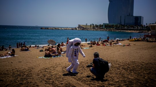 A man films a person dressed as an astronaut on the beach of Barcelona, Spain, where tourist growth has been matched by growing COVID infections.