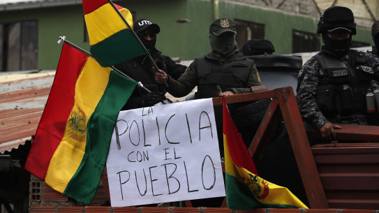 Police against the re-election of President Evo Morales stand on the rooftop of a police station just meters away from the presidential palace waving national flags, near a sign that reads in Spanish: "The police is with the people".