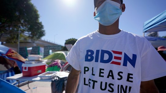 A Honduran man seeking asylum in the United States wears a shirt that reads, “Biden please let us in,” as he stands among tents that line an entrance to the border crossing in Tijuana, Mexico.