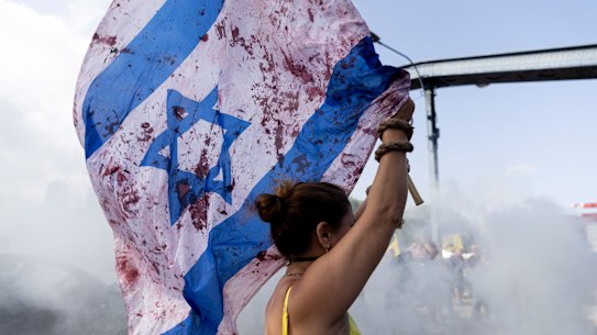 A woman holds an Israeli flag with red paint on it to resemble blood as protesters block a main road during a rally calling for a hostages deal on September 13, 2024 in Tel Aviv, Israel.