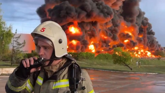 A firefighter speaks on a walkie talkie as smoke and flame rise from a burning fuel tank in Sevastopol, Crimea on Saturday.
