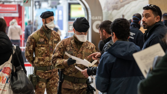 Italian police process passengers leaving from a train station in Milan.