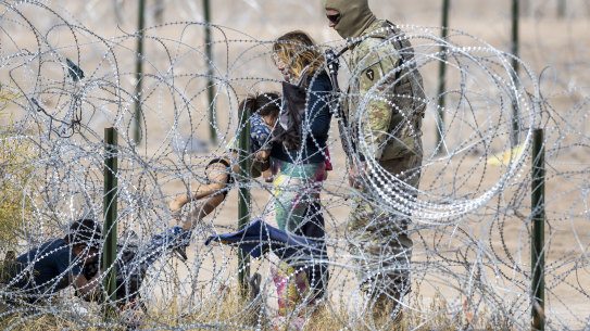 A Texas National Guardsman looks on as a family pulls through razor wire after crossing the Rio Grande into El Paso, from Ciudad Juarez, Mexico.