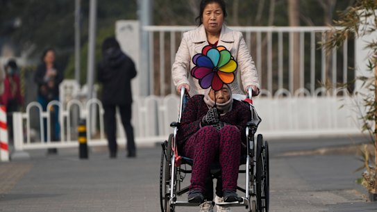 A woman pushes an elderly woman holding a rainbow fan on a street in Beijing. 