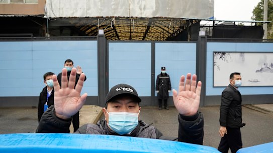 A security guard waves for journalists to clear the road after a convoy carrying the World Health Organisation team entered the Huanan Seafood Market in January 2021.