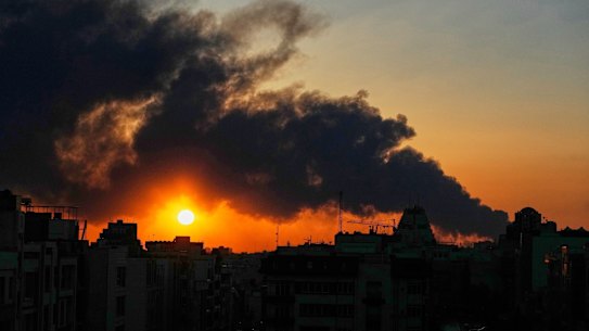 The sun sets behind a plume of smoke rising after a US-Israeli military strike in Tehran, Iran’s capital.
