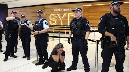 A supporter of the Iranian women’s soccer team is crouched in distress at the knees of police officers in Sydney International Airport.