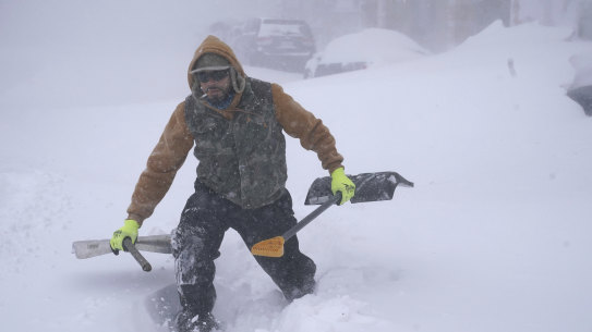 Travis Sanchez trudges over a snowdrift with a pair of shovels for a stranded motorist on Chenango Street in Buffalo, NY. 