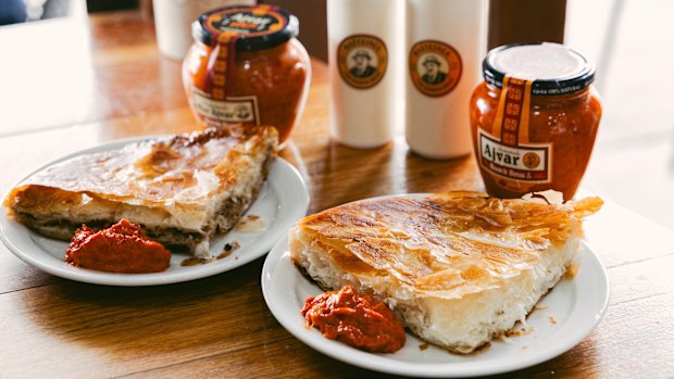 A slice of meat burek and cheese burek, served with buttermilk drink and ajvar.