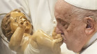Pope Francis kisses a wooden statuette of the infant Jesus.