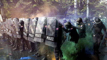 Riot police stand in formation as pro-democracy protesters throw smoke bombs.