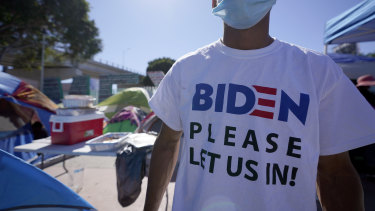 A Honduran man seeking asylum in the United States wears a shirt that reads, “Biden please let us in,” as he stands among tents that line an entrance to the border crossing in Tijuana, Mexico.