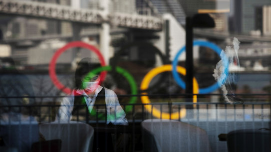 The Olympics rings are reflected on the window of a hotel restaurant as a server with a mask sets up a table in the Odaiba section of Tokyo.