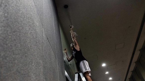 A protester uses spray paint to cover the lens of a security camera after demonstrators breached the doors of the Legislative Council in Hong Kong on July 1. A quest to identify protesters and police officers has people in both groups desperate to protect their anonymity. 