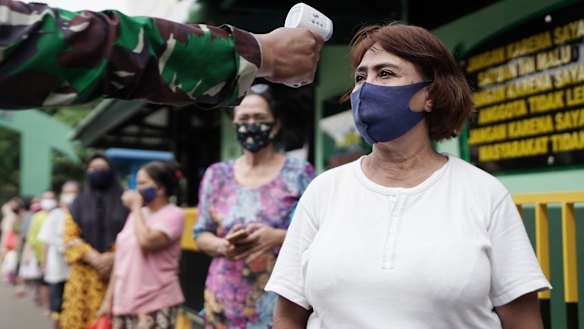A soldier takes the temperature of a person following social distancing protocols while waiting in line at a rice distribution center at the Central Jakarta Military District Command.