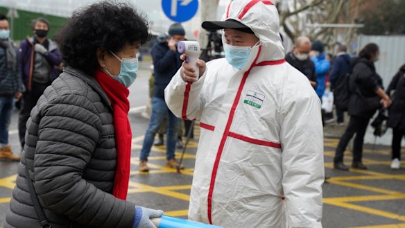 A worker in protective overalls takes the temperature of a woman entering the Hubei Centre for Disease Control and Prevention as the World Health Organisation team makes a visit.