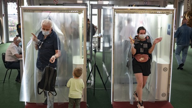 People wearing face masks and gloves to protect against coronavirus come through passages equipped with disinfectant sprays at a shopping mall entrance in Moscow, Russia.