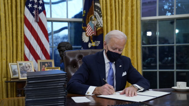 President Joe Biden signs his first executive orders in the Oval Office of the White House.