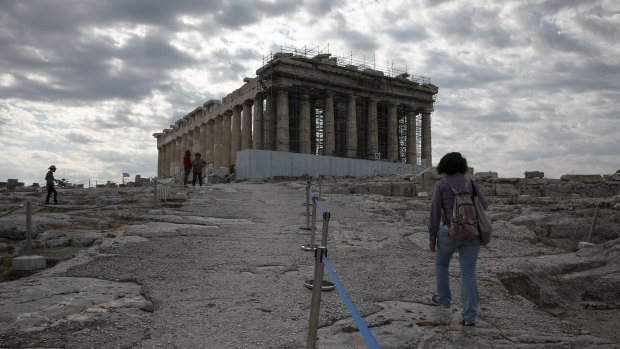 An employee of the Greek Culture Ministry walks alongside a belt separating visitors into sections at the archaeological site of the Acropolis in Athens.