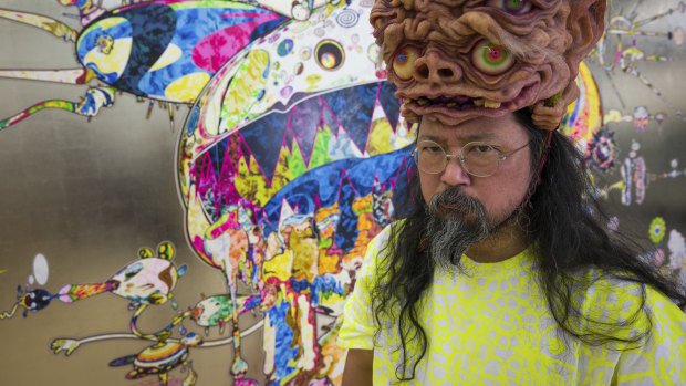 Takashi Murakami, wearing a headpiece from  Amazing Studio JUR, in front of his artwork Tan Tan Bo Black Hole (2019).