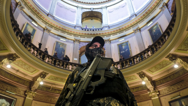 An armed protester wearing a mask stands at the Michigan Capitol Building in Lansing, Michigan.