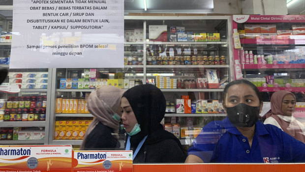 Employees wait for customers at a counter displaying a notification saying that the sale of medicinal syrup is temporarily halted at a pharmacy in Jakarta.