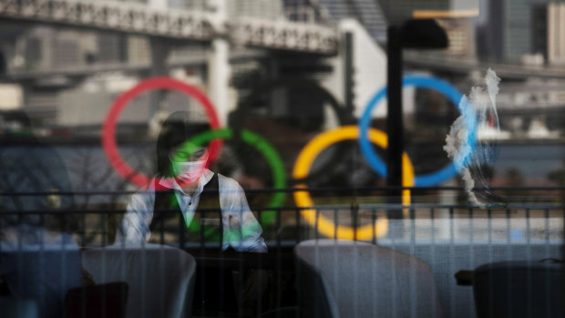 The Olympics rings are reflected on the window of a hotel restaurant as a server with a mask sets up a table in the Odaiba section of Tokyo.