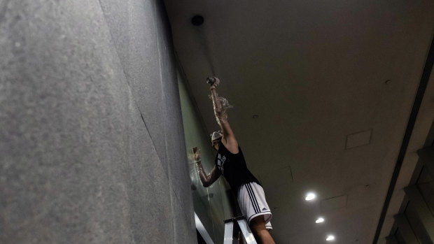 A protester uses spray paint to cover the lens of a security camera after demonstrators breached the doors of the Legislative Council in Hong Kong on July 1. A quest to identify protesters and police officers has people in both groups desperate to protect their anonymity. 